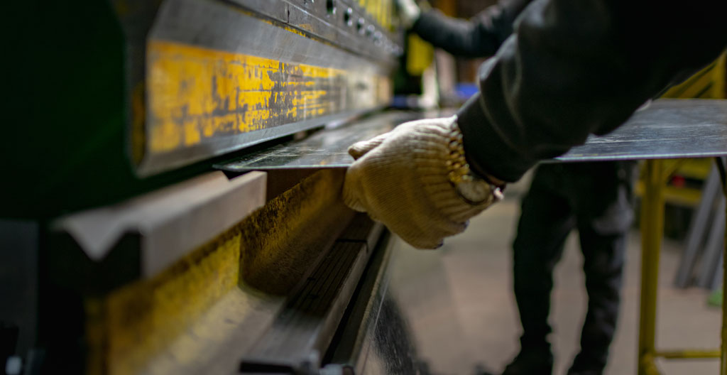 Des mains gantées manipulent une plieuse métallique avec une bande de zinc en cours de pliage