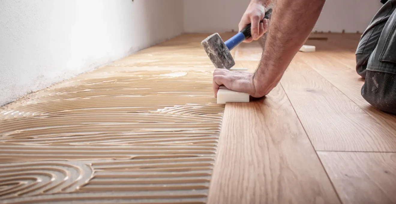 Un professionnel de plancher installe une nouvelle lame de bois d'ingénierie sur un sous-plancher exposé lors d'une réparation.