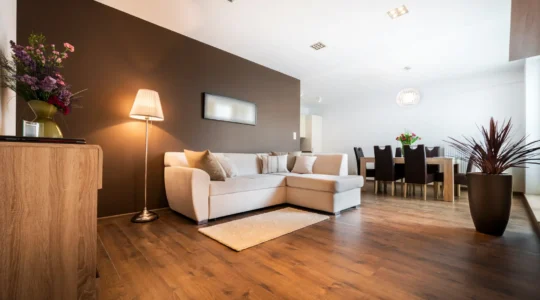 Un technicien mesure l'humidité d'un plancher de bois franc gondolé par un dégât d'eau dans un salon résidentiel.